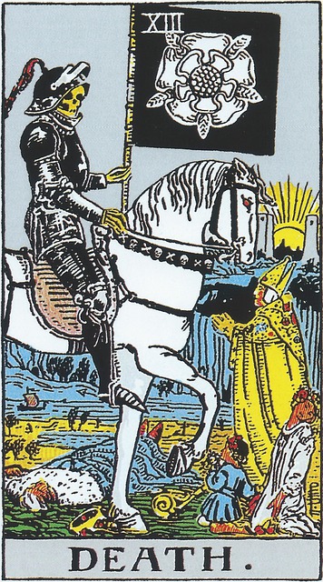 Tarot cards Death
A figure in black armor, face that of a skeleton, rides a white horse with glowing red eyes. A red feather wilts from the peak of his helm. The chest stall of the horse is decorated with skull and crossbones. In his left hand is a black standard bearing the image of a white flower and five ears of corn, or wheat.  There is a king lying dead beneath the hooves of his horse, his crown fallen to the ground, and his scepter lying next to him.  The land is barren, there is a tiny ship on the seas in the distance.  On the ground is a baby in blue, and a maiden in white, both kneeling in supplication.  At the head of the horse stands a pope, hands clasped in prayer, with dark shadows stretching out from him.  In the distance we see two towers, with the sun setting or rising between them
