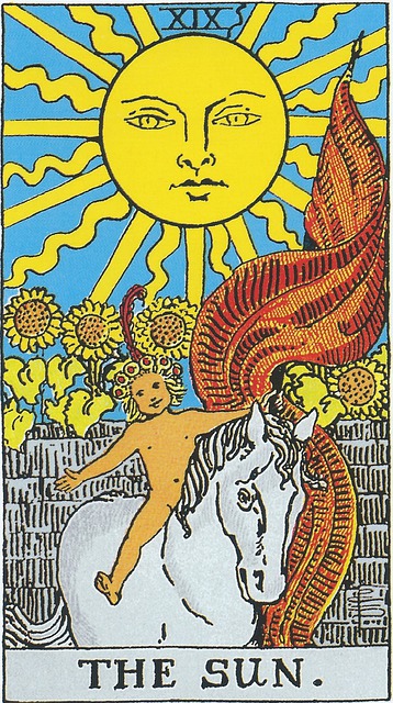 19. The Sun Tarot Card
A smiling naked child with opens arms wearing a garland of flowers crowned by a red feather, carries a red banner, while riding a white horse.  Behind is a wall separating him from a field of tall sunflowers. Overlooking the scene is a large sun, lending warmth and light.
